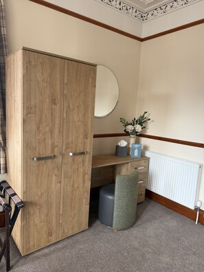 A room with a wooden wardrobe, a round mirror, a small desk with a plant, and a radiator. - The Famous Star Hotel (Moffat)