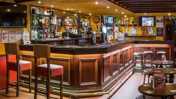Un espace bar avec un comptoir en bois, des tabourets et une variété de bouteilles et de verres.