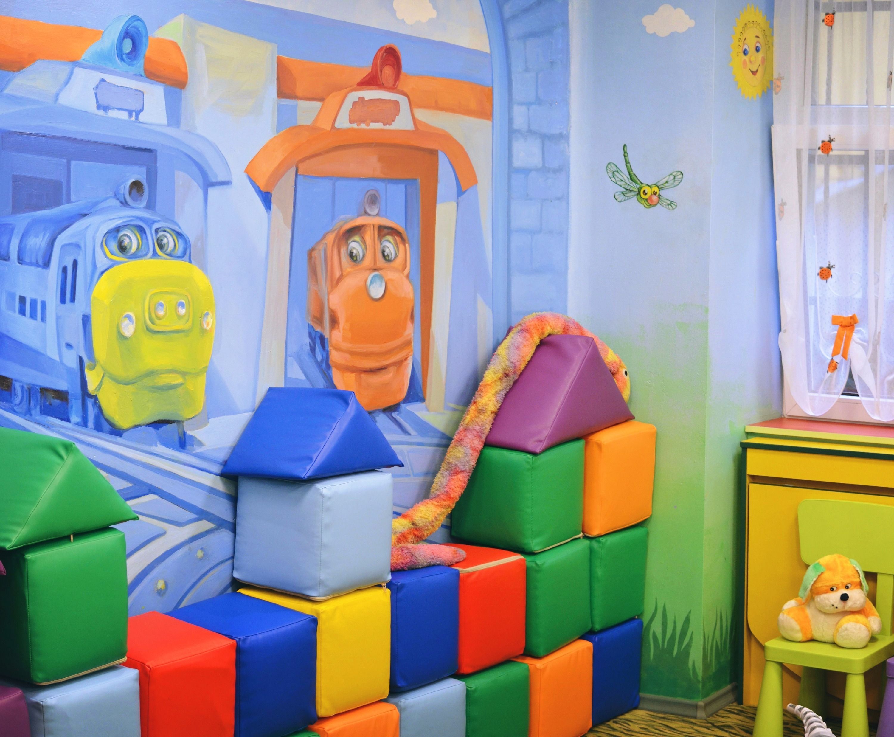 A children's playroom with colorful blocks, a train mural, and a toy train on a shelf.