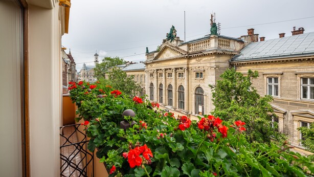 Un balcón con flores rojas y vistas a un edificio histórico de arquitectura clásica.