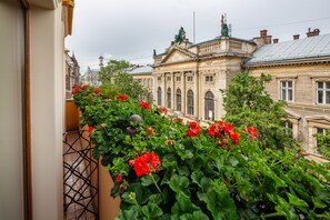 A balcony with red flowers and a view of a historic building with classical architecture. - Swiss Hotel (Lviv)