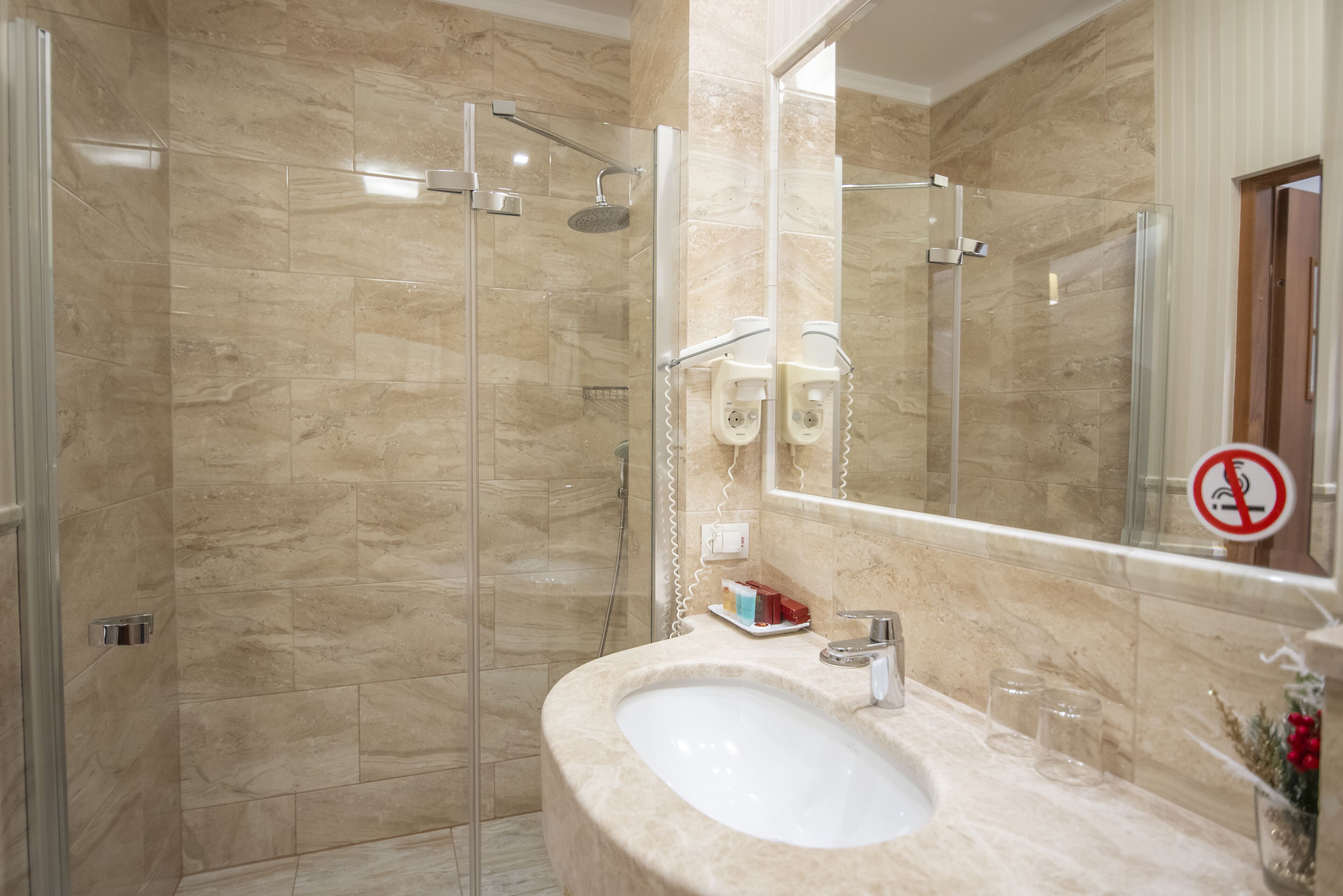 Une salle de bain avec une douche à parois de verre, un lavabo avec un miroir et un panneau indiquant qu'il est interdit de fumer.