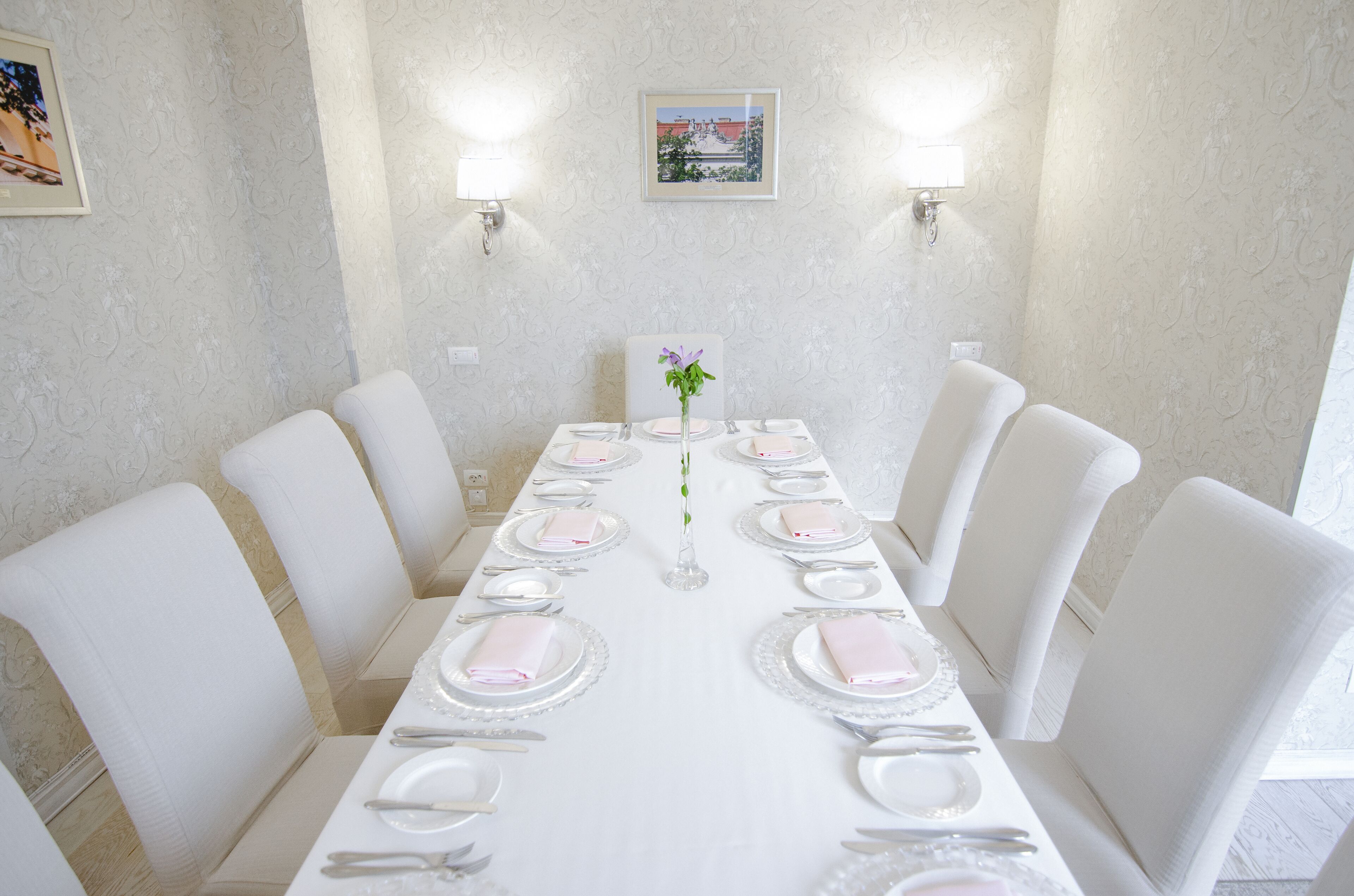 Un comedor con una mesa larga dispuesta para una comida, sillas blancas e iluminación empotrada en la pared.