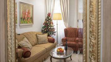 Een woonkamer met een beige bank, een kerstboom, een lamp en een klein tafeltje met fruit.