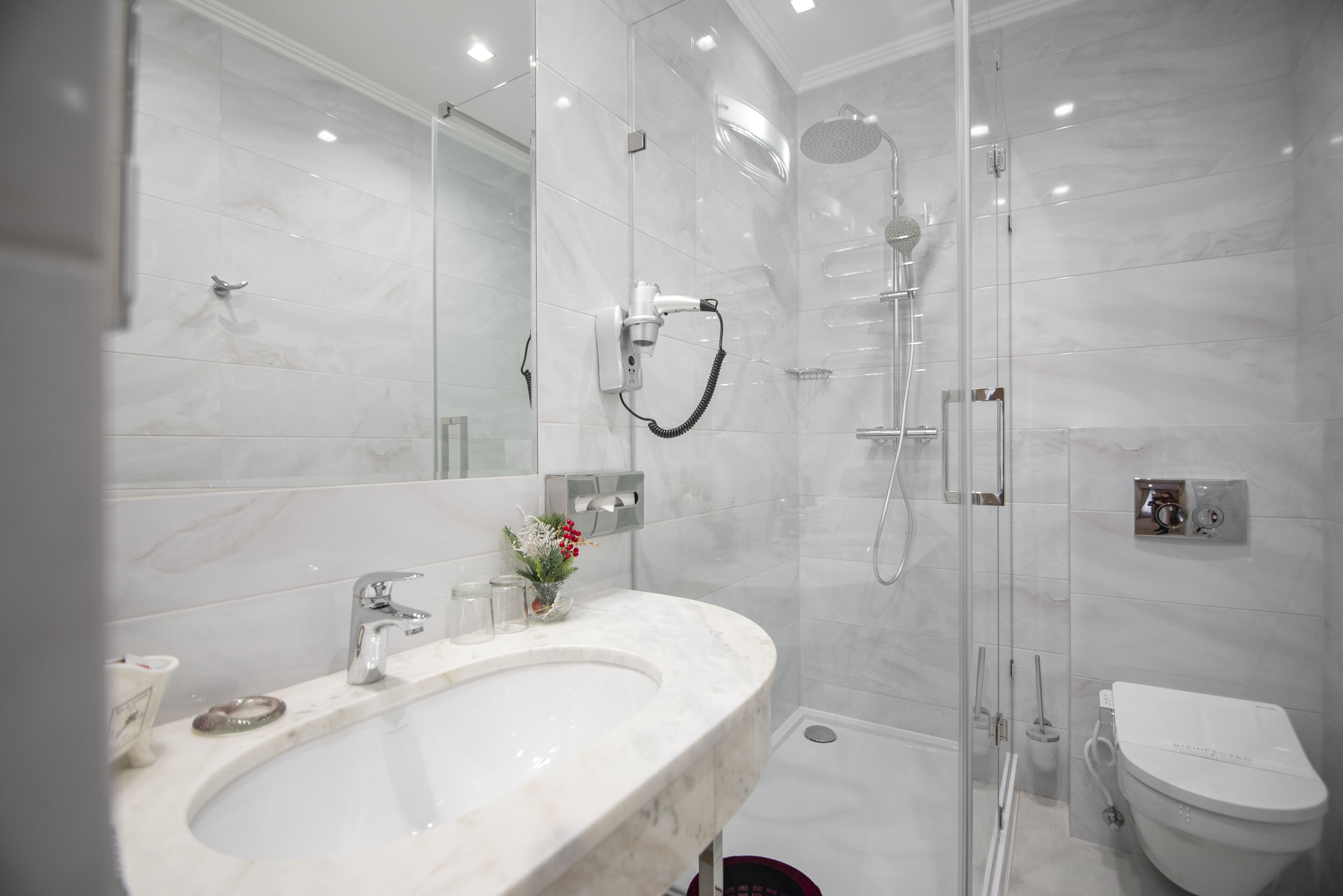 A modern bathroom with a marble sink, glass-enclosed shower, and a toilet.