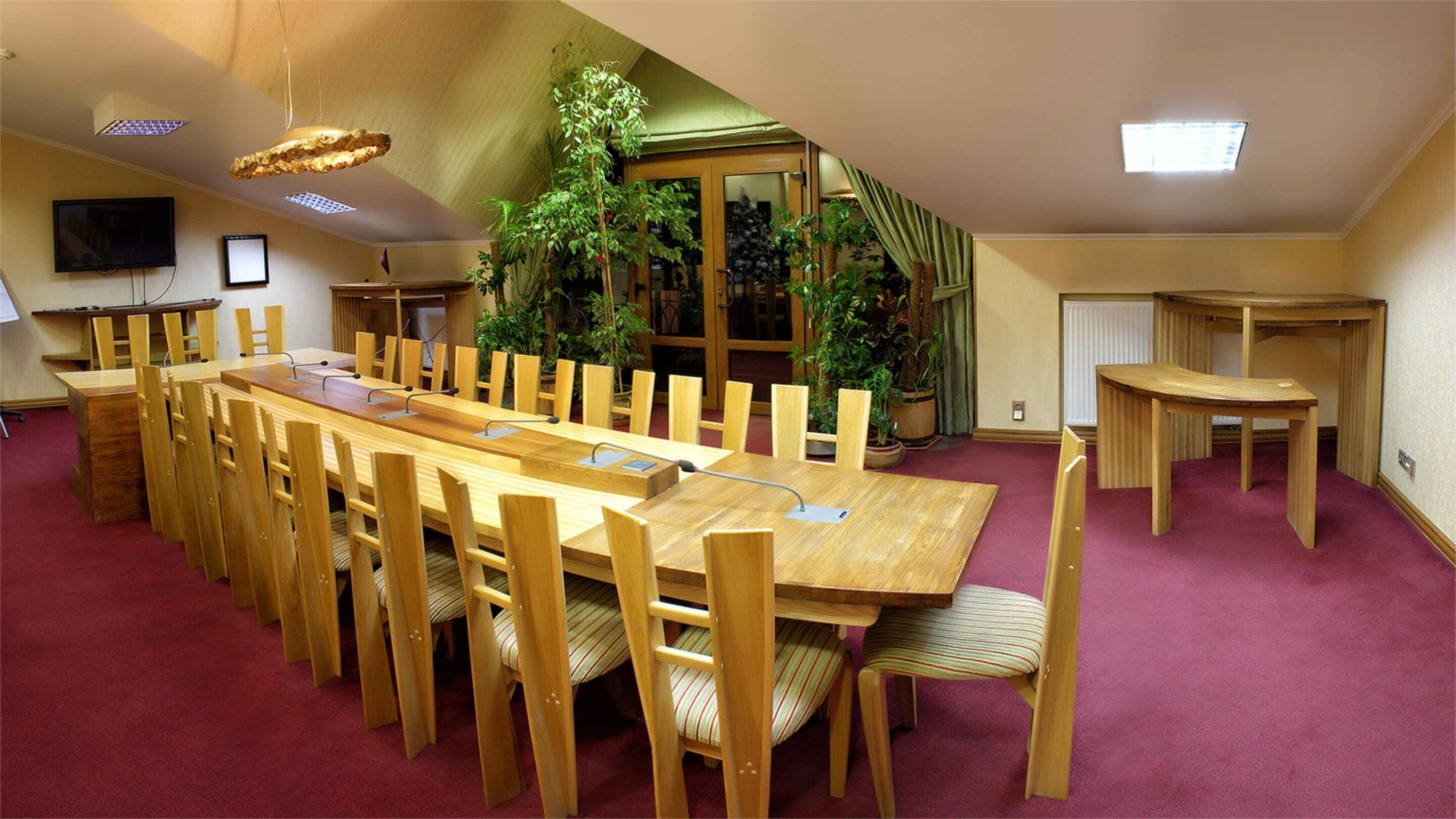 A conference room with a long wooden table and chairs, a television, and potted plants.