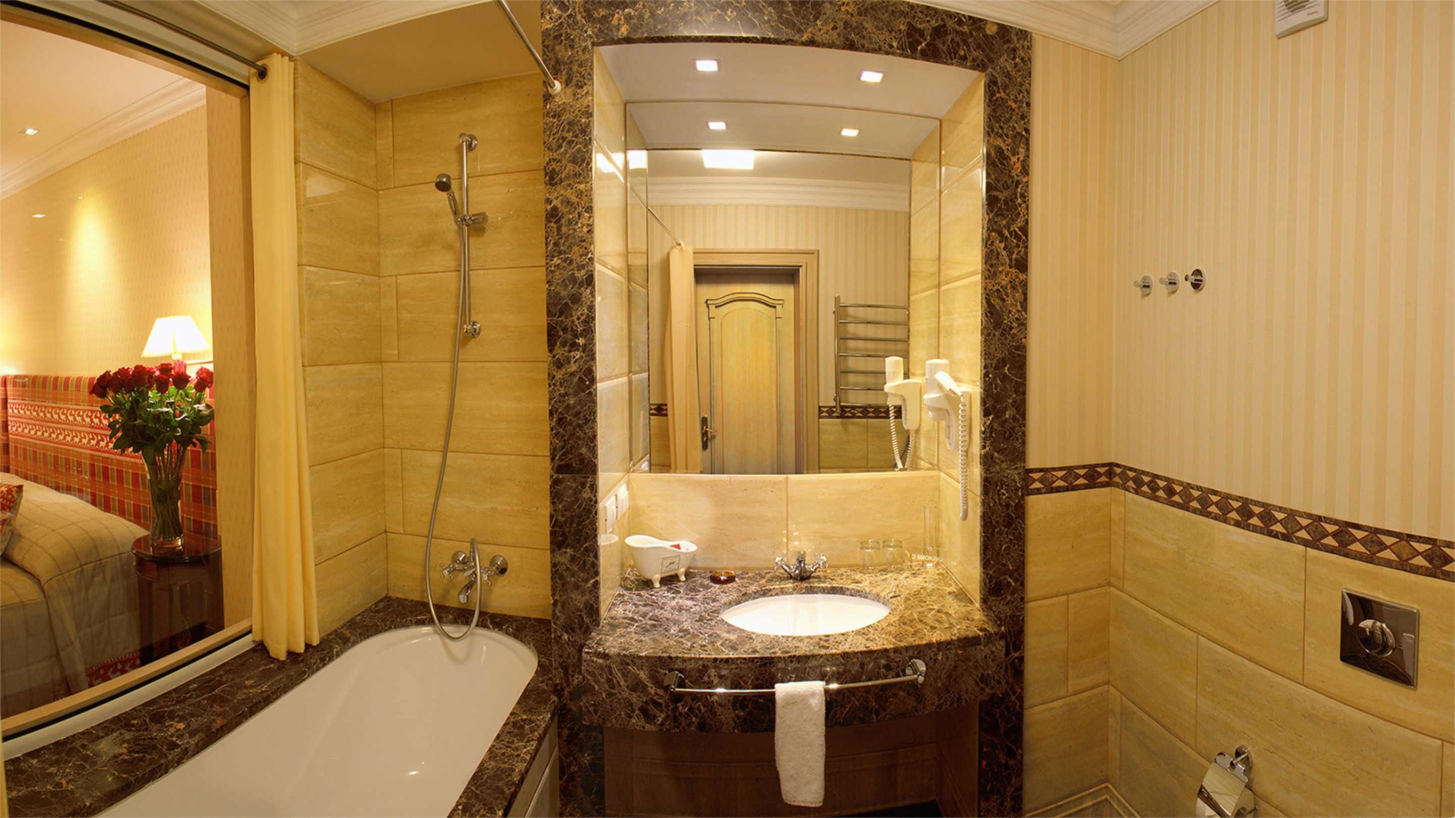 A bathroom with a bathtub, a sink, and a shower. There is a mirror above the sink and a towel hanging on the wall.