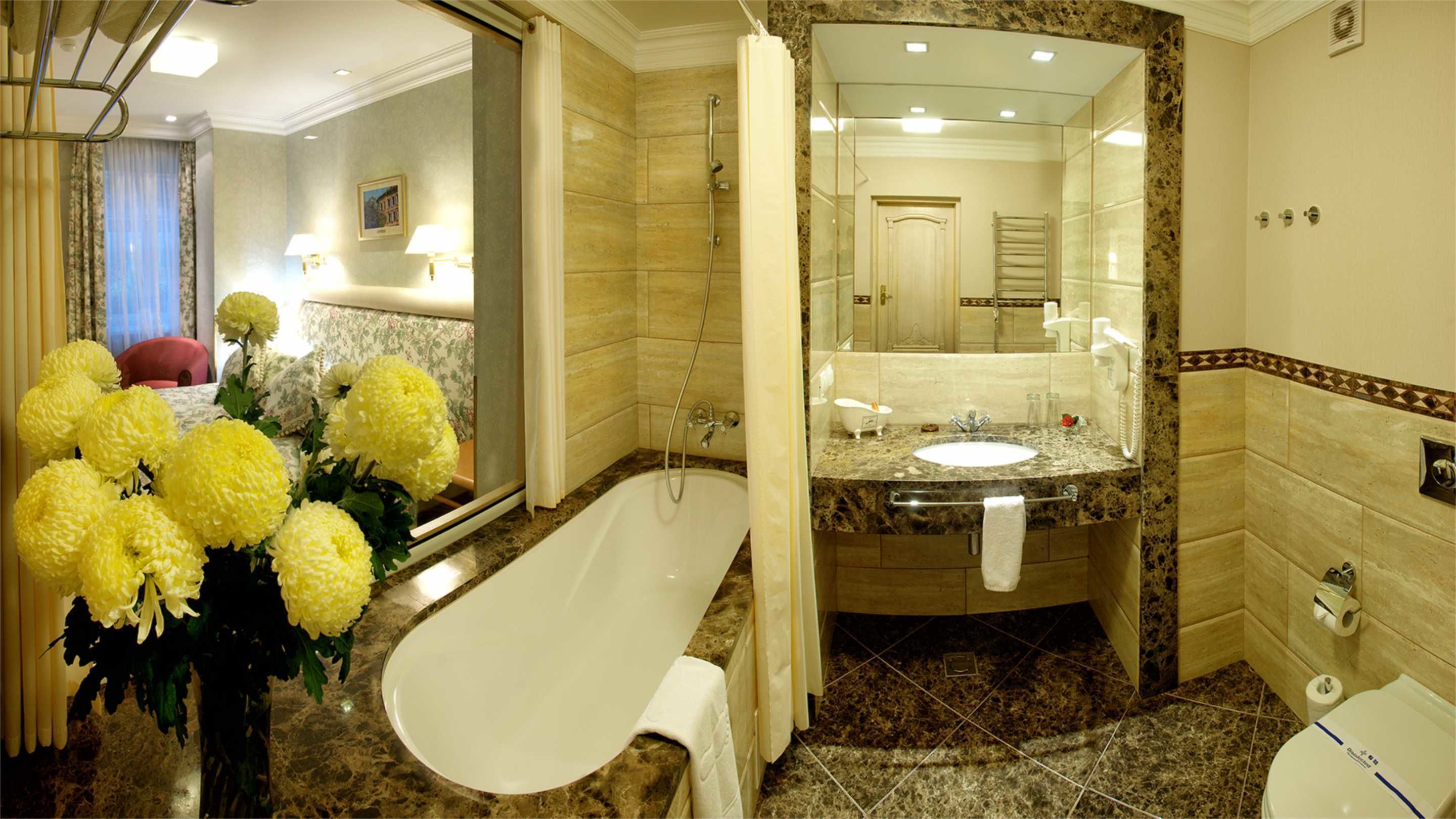 Un baño con bañera, lavamanos e inodoro. Hay un espejo sobre el lavamanos y una cortina de ducha.