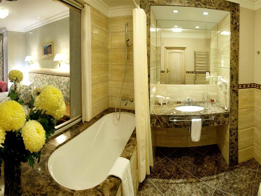 Un baño con bañera, lavamanos e inodoro. Hay un espejo sobre el lavamanos y una cortina de ducha.