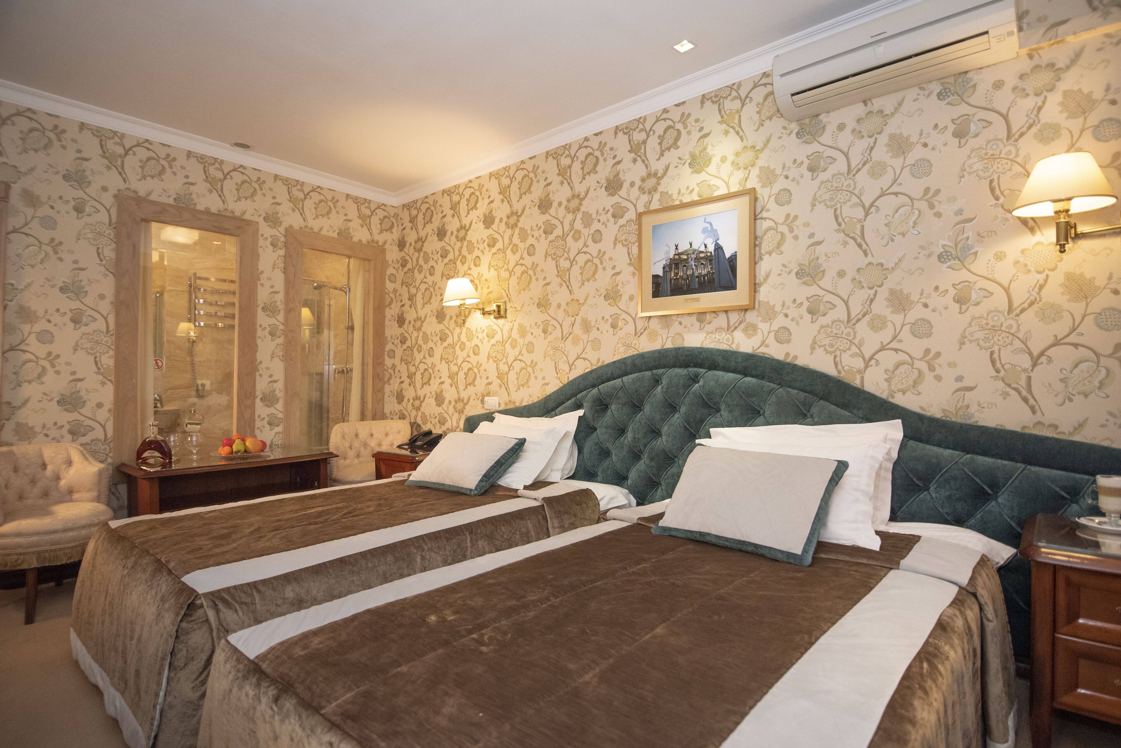 A hotel room with a large bed, two bedside tables, a chair, and a wall-mounted air conditioner.