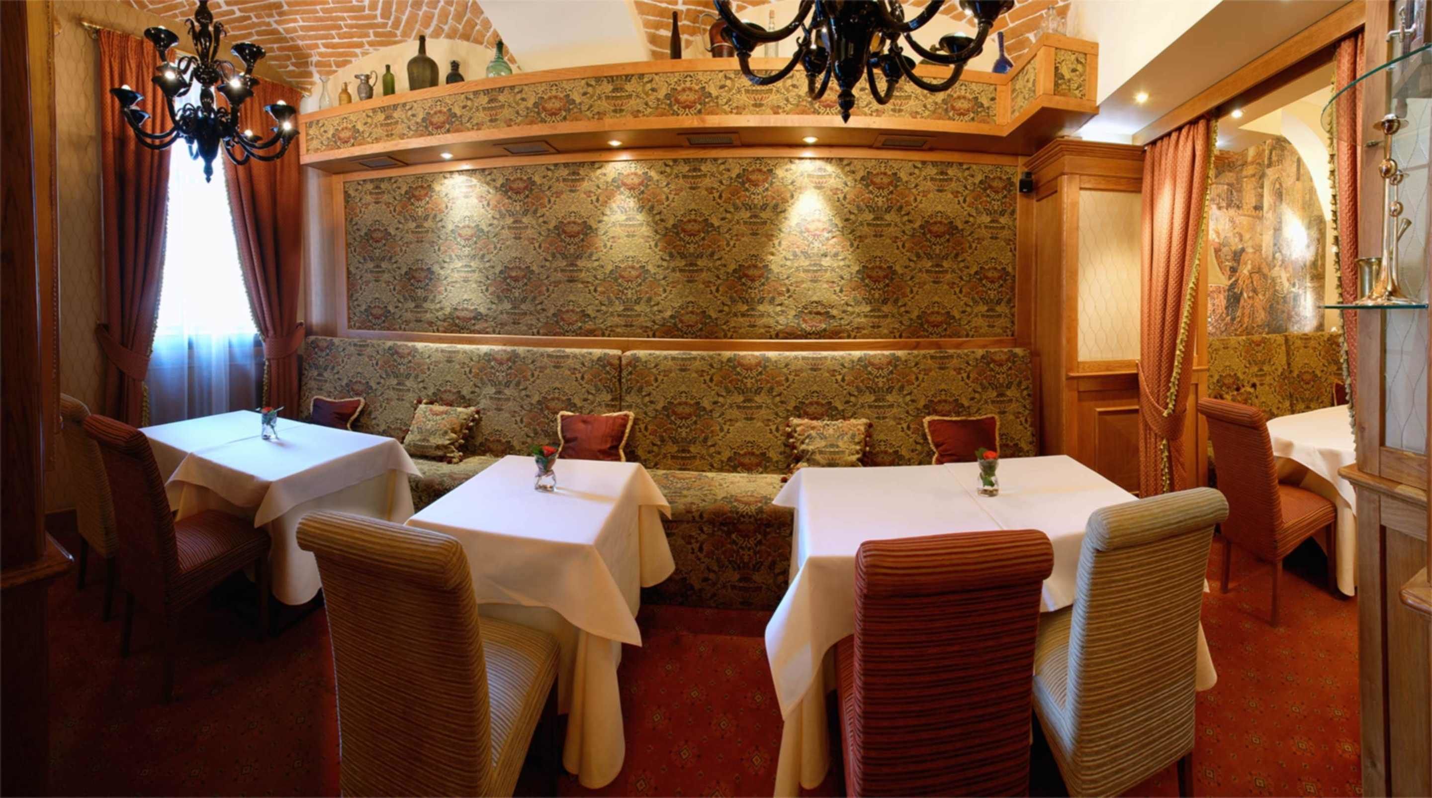 A restaurant with a traditional interior, featuring a patterned wall, wooden furniture, and a chandelier.