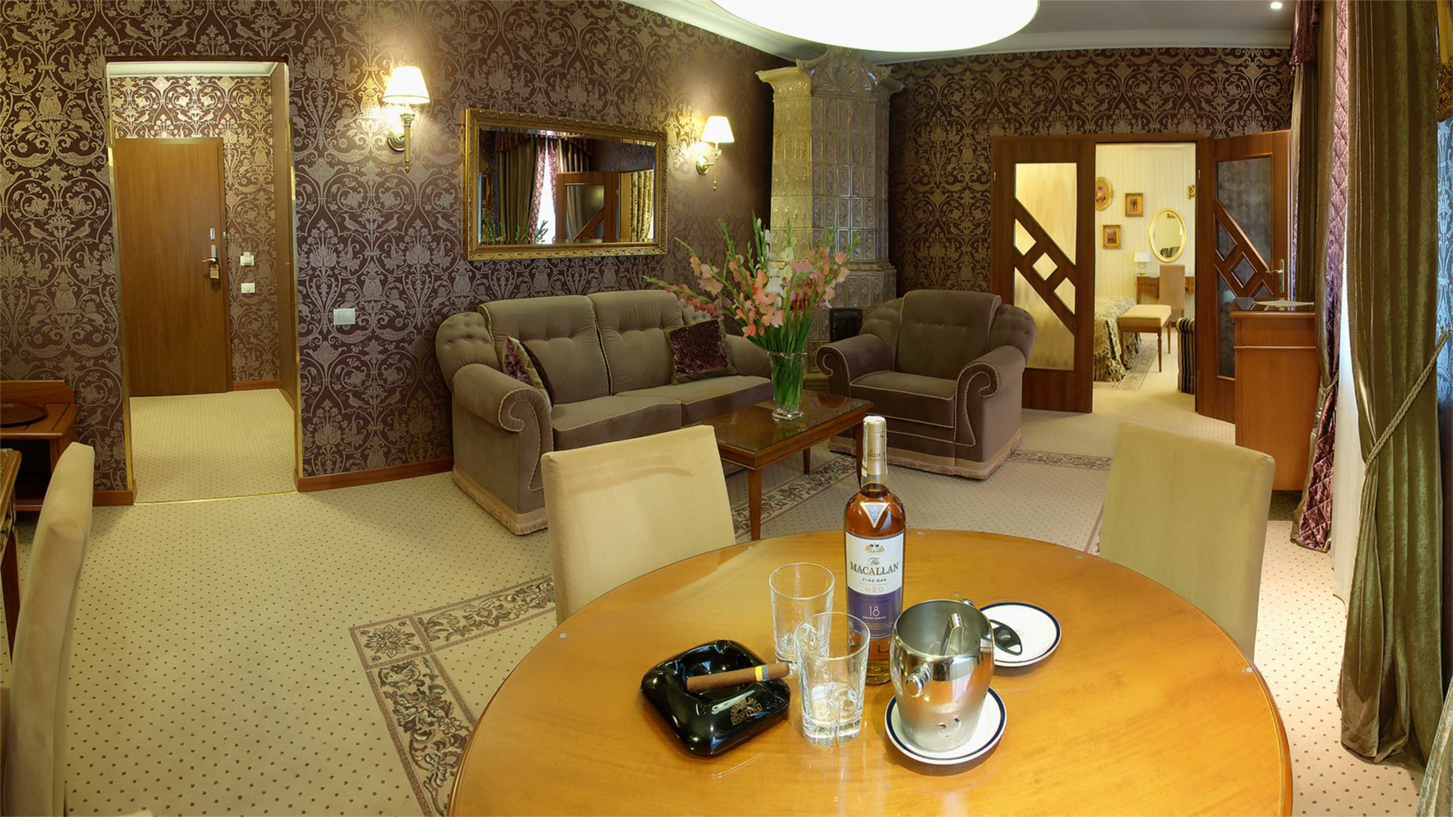 A living room with a sofa, armchairs, a coffee table, and a dining table with chairs. There is a bottle of wine, a glass, and an ashtray on the table.