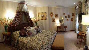 A hotel room with a four-poster bed, a desk, a chair, and a vanity with a mirror.