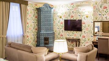 A living room with beige sofas, a table with a lamp, a blue cabinet, and floral wallpaper.