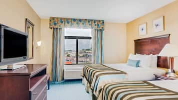 Habitación de hotel con dos camas, televisión, cómoda y ventana con vista a la ciudad.