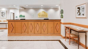 Un comptoir d’accueil avec une enseigne indiquant « Wingate by Wyndham » et une œuvre d’art florale encadrée accrochée au mur.