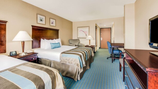 Une chambre d’hôtel avec deux lits, un bureau, une chaise, une télévision et une salle de bain visible à travers une porte ouverte.