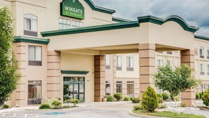 Un hôtel à la façade verte et beige, avec une enseigne bien visible indiquant « Wingate by Wyndham », et un espace d’entrée abrité donnant sur un parking.