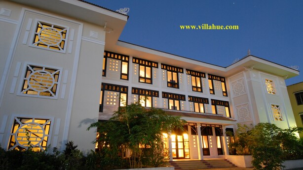 A multi-story building with traditional architectural features, including decorative windows and a well-lit entrance. - Villa Hue (Hue)