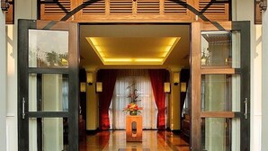 A hotel entrance with a modern design, featuring a central reception desk, red curtains, and a decorative vase with flowers. - Villa Hue (Hue)