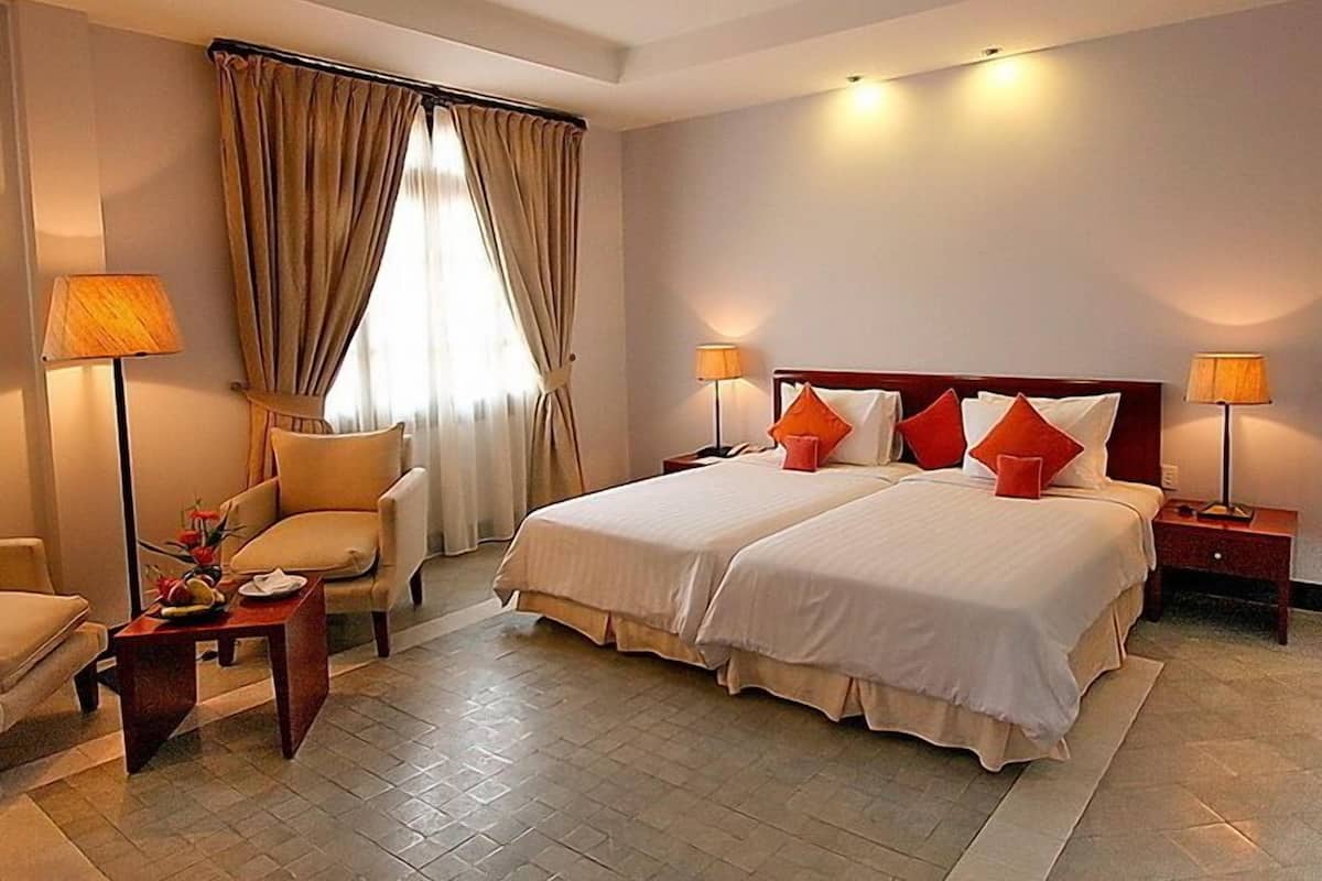 Una habitación de hotel con dos camas, una silla, una mesa y una lámpara.