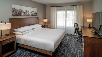 Una habitación de hotel con una cama grande, dos mesitas de noche con lámparas, un escritorio con una silla y una ventana con cortinas.