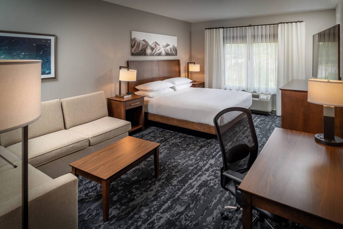 A hotel room with a bed, a sofa, a desk, and a chair. There are two bedside tables with lamps.