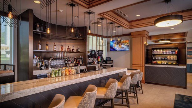 A bar area with a marble countertop, bar stools, and a variety of liquor bottles. - Delta Hotels by Marriott Huntington Mall (Barboursville)