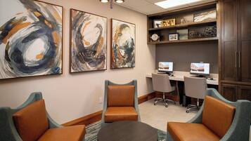 Uma sala de conferências com duas poltronas de couro, uma mesa pequena e quadros abstratos nas paredes.