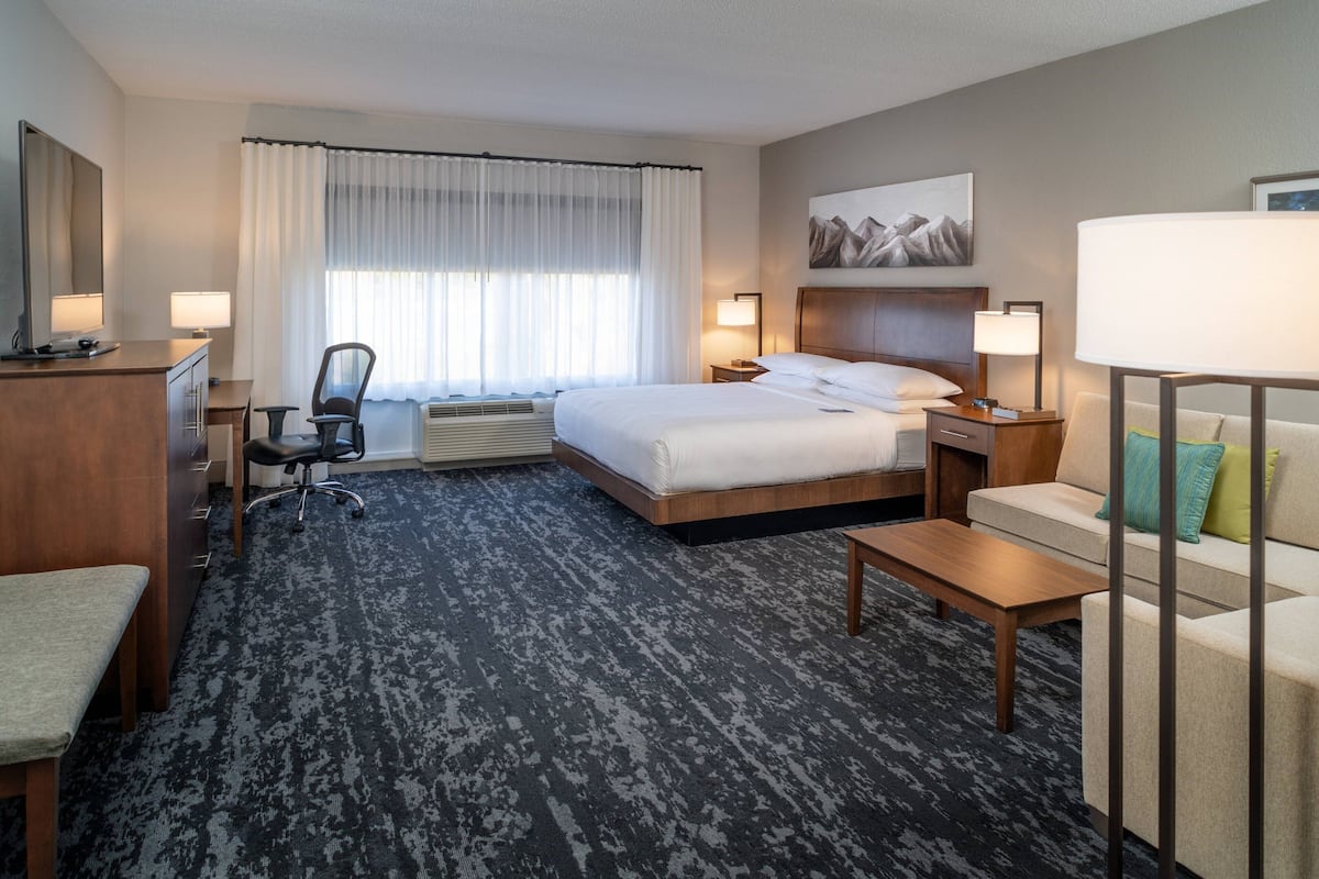 A hotel room with a bed, desk, chair, and a sofa.