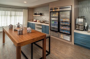 Una cocina moderna con una mesa de madera, un refrigerador lleno de bebidas y una cafetera.