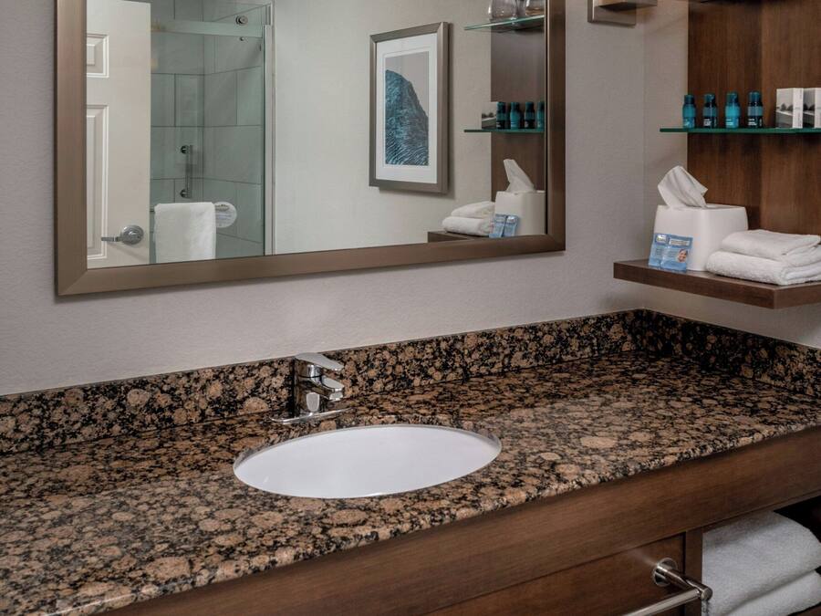 A modern bathroom with a granite countertop sink, a large mirror, and a wooden vanity with a towel rack.