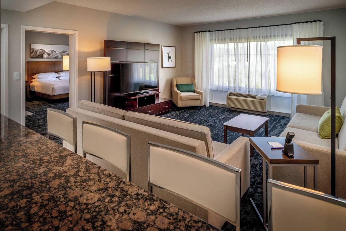 A hotel room with a bed, TV, seating area, and a desk with a lamp.