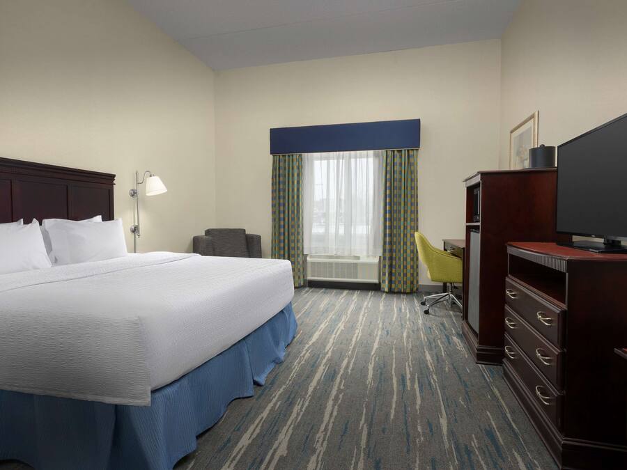 Habitación de hotel con una cama grande, un escritorio, una silla, un televisor y una ventana con cortinas.