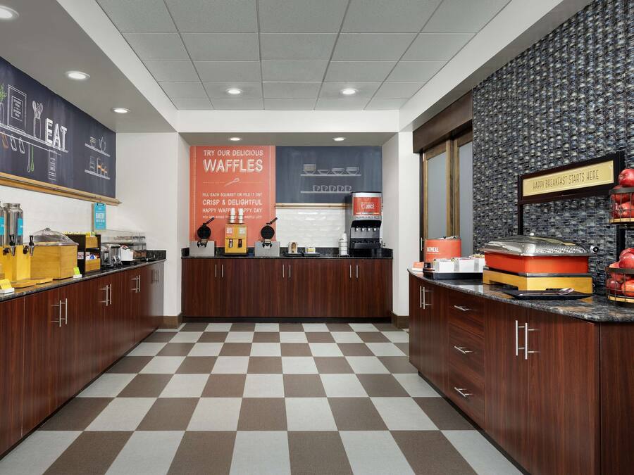 A modern kitchen area with a checkered floor, wooden cabinets, and a waffle station.