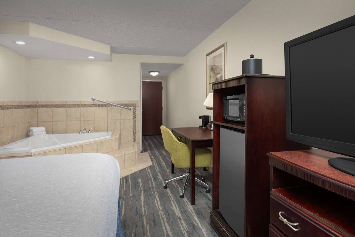 A hotel room with a bed, a desk, a chair, a television, and a bathroom with a bathtub and shower.