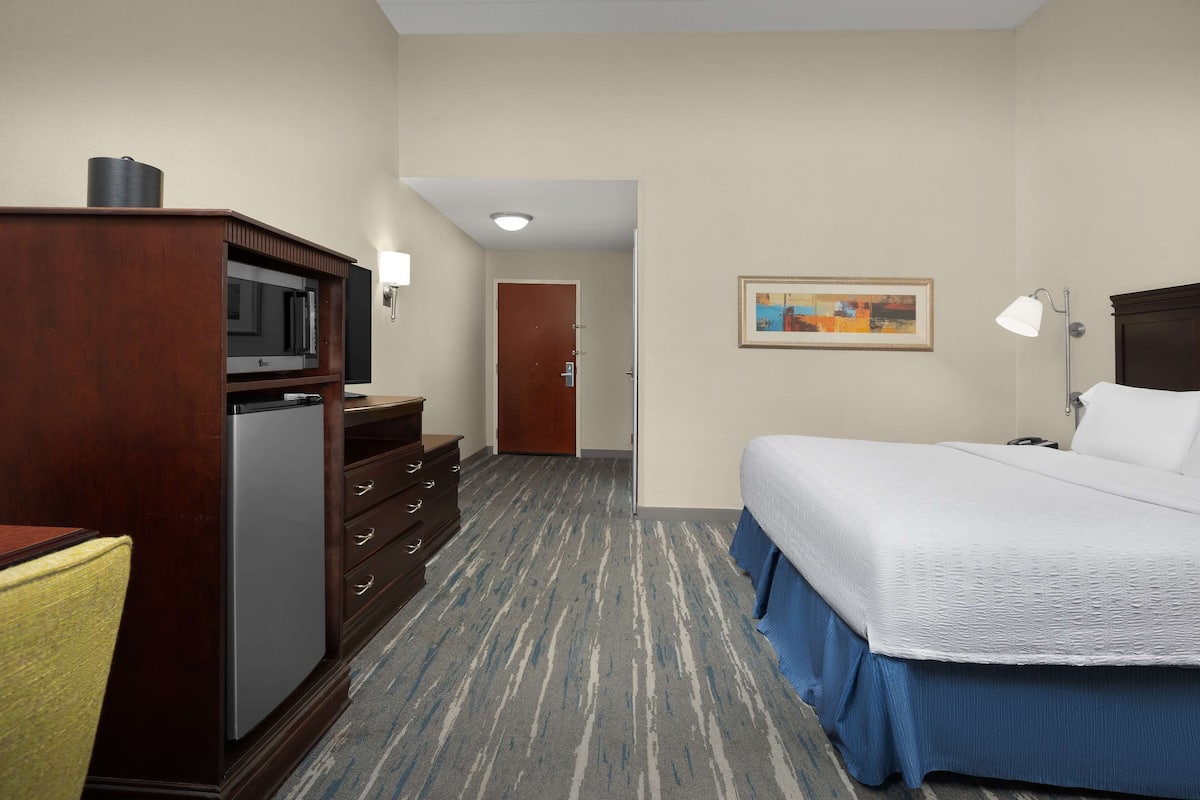A hotel room with a bed, a desk with a television, a dresser, and a door leading to another room.