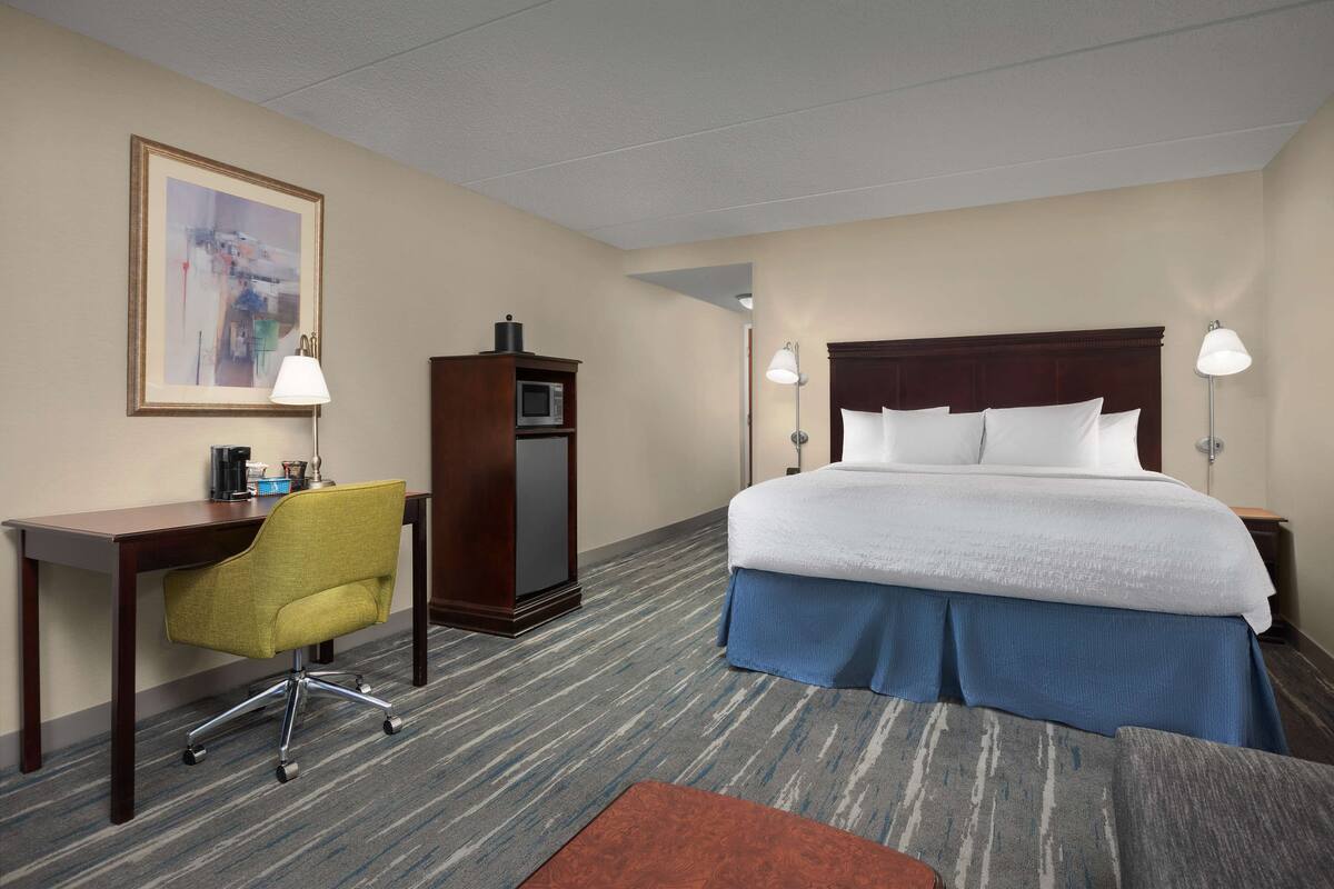 A hotel room with a bed, desk, chair, and a television.