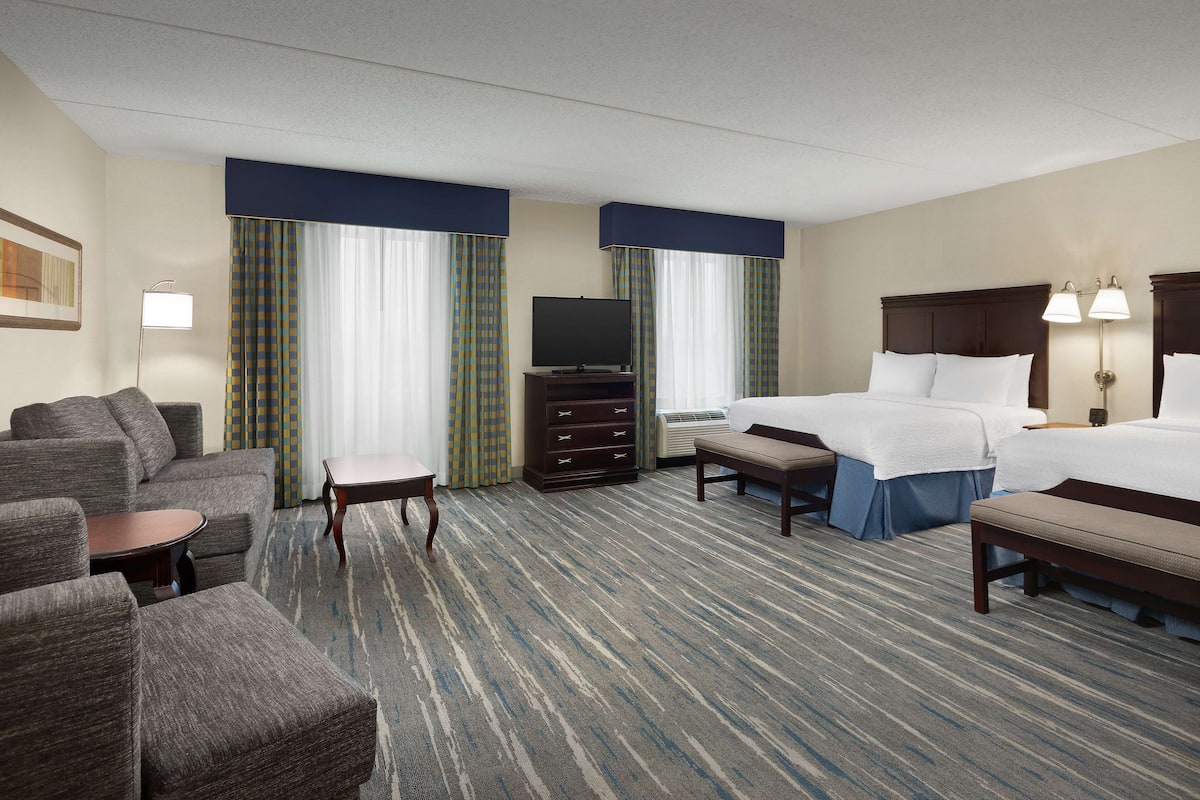 A hotel room with a sofa, two beds, a TV, a dresser, and a carpeted floor.