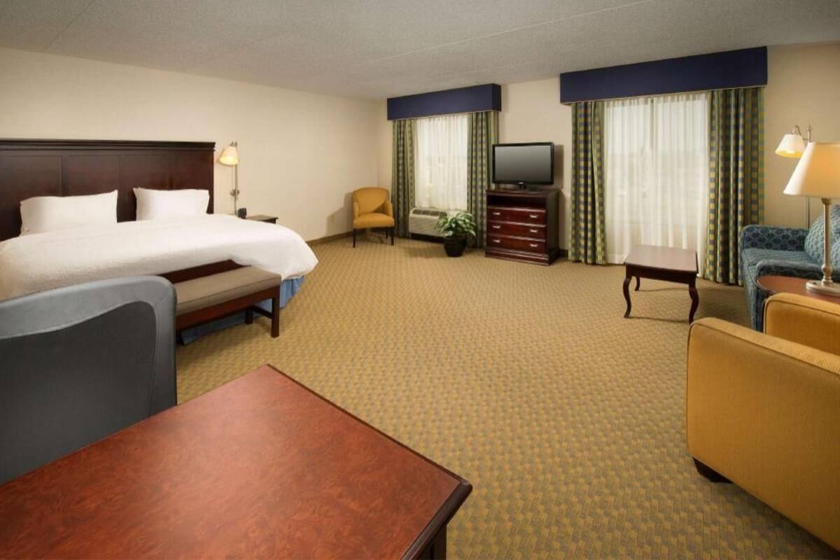 A hotel room with a bed, a desk, a chair, a television, a sofa, and a small table.
