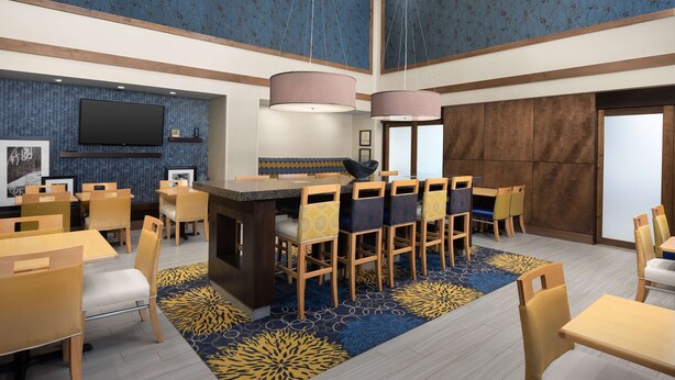 A modern dining area with a central bar, wooden chairs, and a patterned carpet.