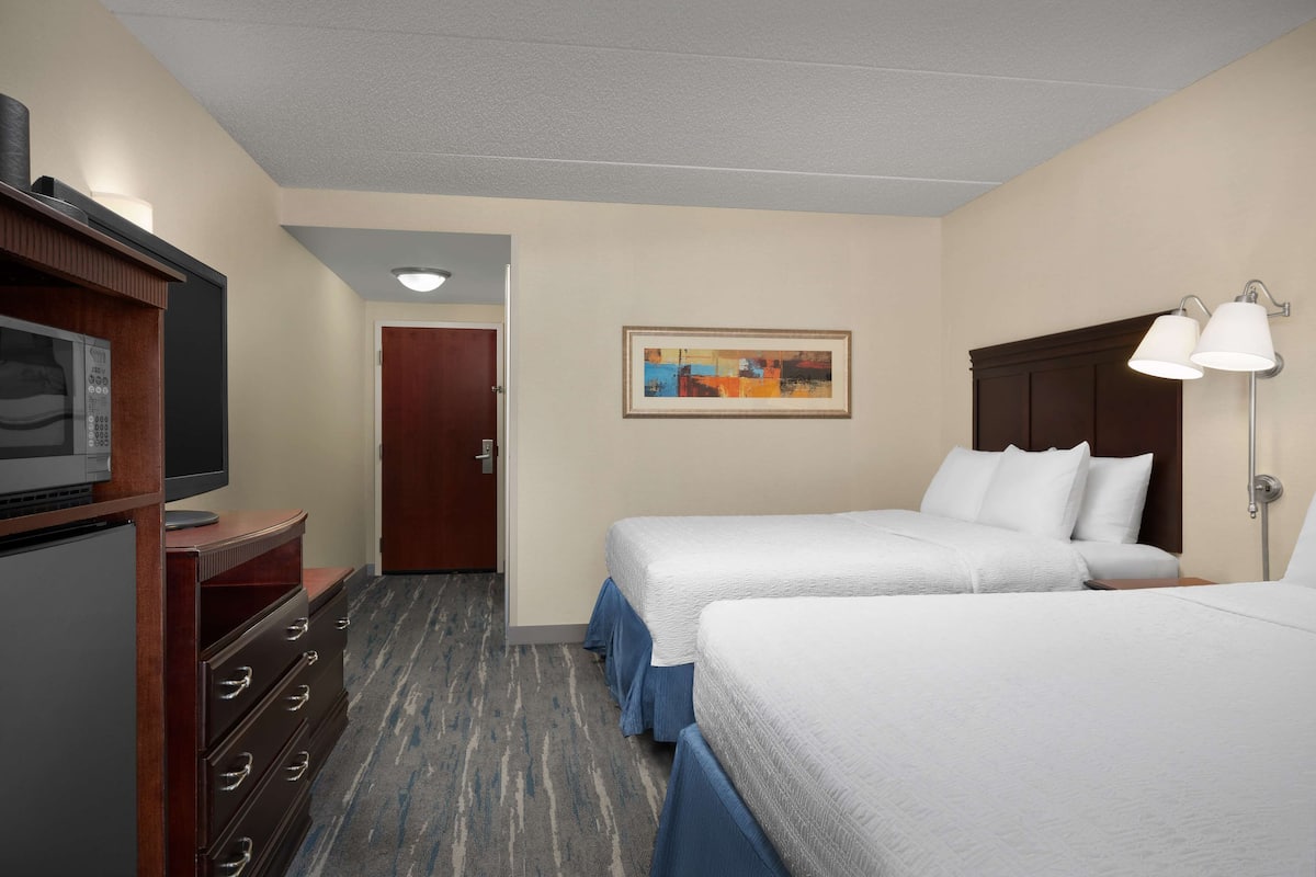 A hotel room with two beds, a desk with a television, a dresser, and a painting on the wall.