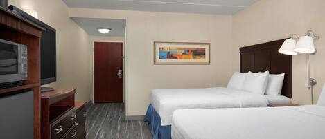 Ein Hotelzimmer mit zwei Betten, einem Schreibtisch mit Fernseher, einem Schminktisch und einem Bild an der Wand.