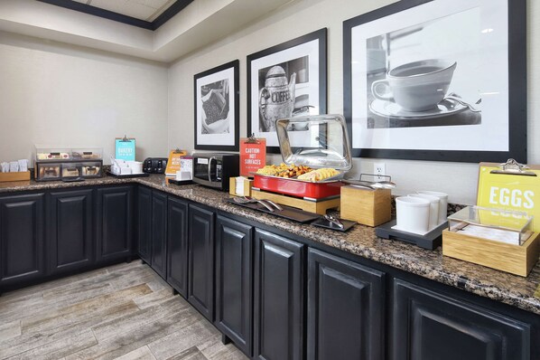 A kitchen with dark cabinets, a granite countertop, a coffee station, and framed pictures on the wall.