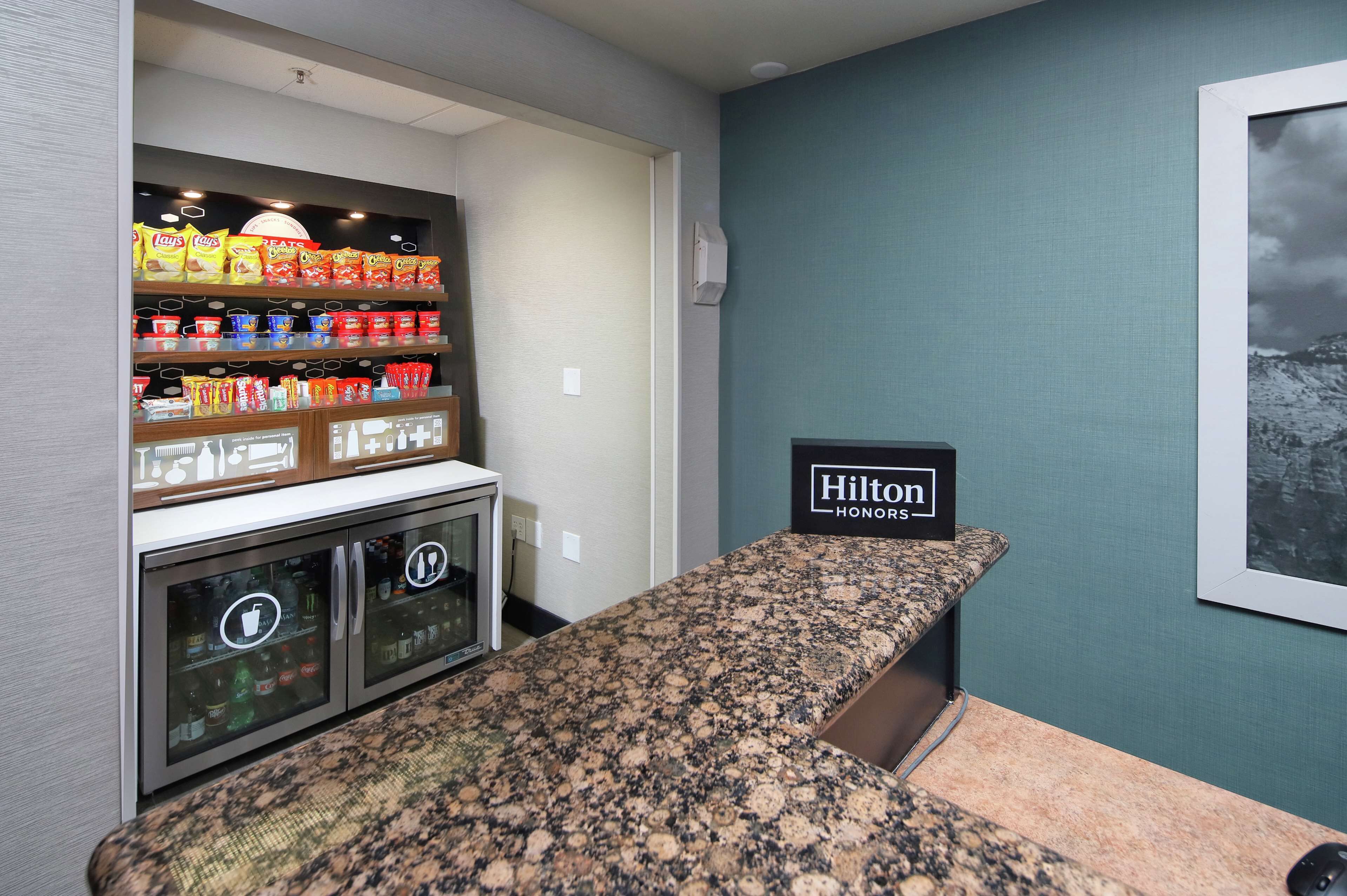 A kitchenette with a granite countertop, a minibar with snacks, and a sign indicating it's a Hilton Honors hotel.