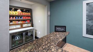 A kitchenette with a granite countertop, a minibar with snacks, and a sign indicating it's a Hilton Honors hotel.
