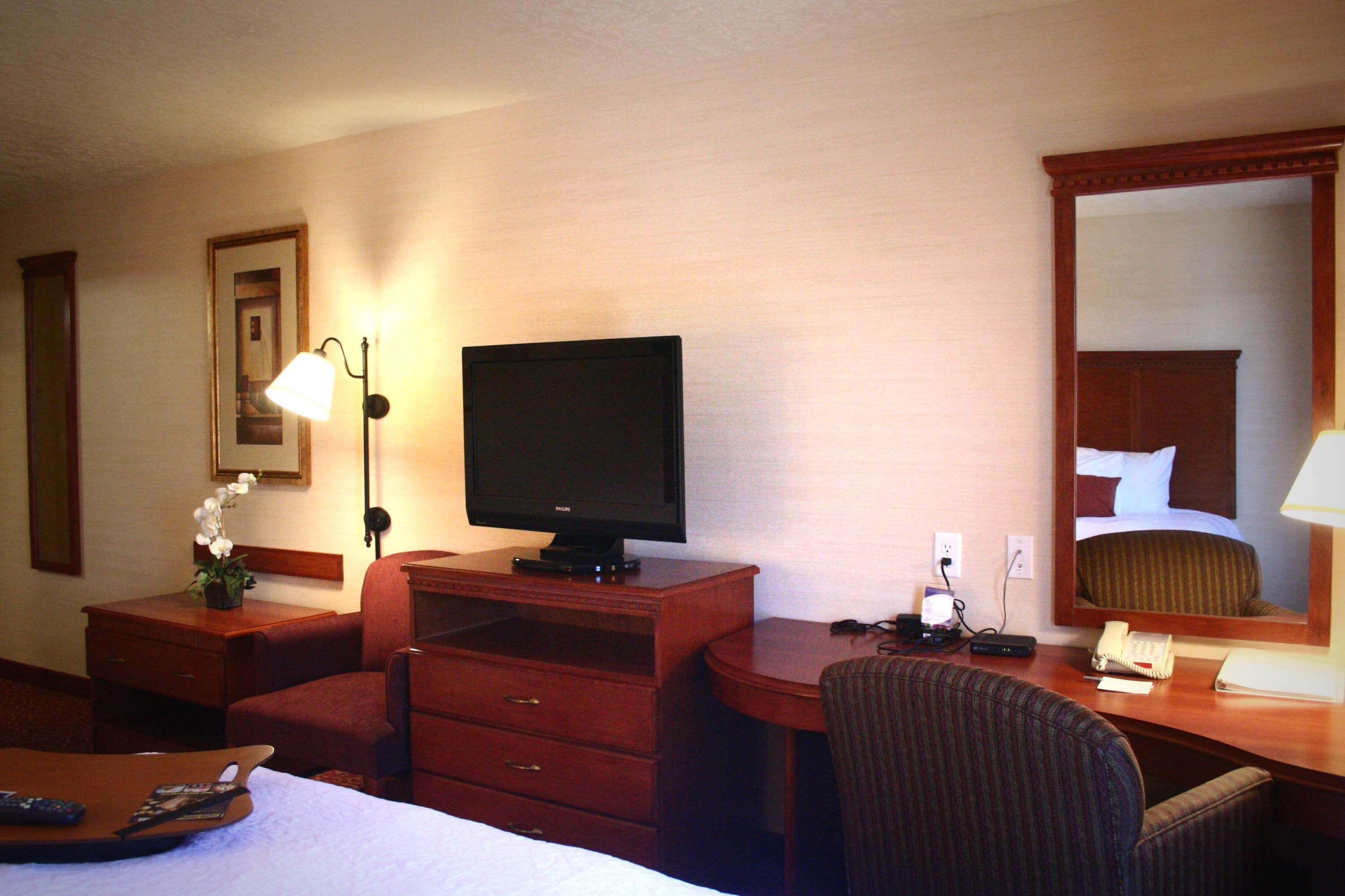 A hotel room with a bed, a desk with a computer, a chair, a dresser, a lamp, and a television.