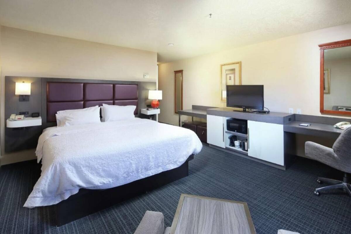 A hotel room with a bed, a desk, a chair, a television, and a mirror.