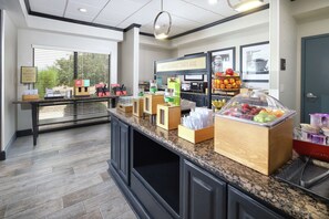 A breakfast area with a counter, food display, and a sign indicating breakfast starts here.