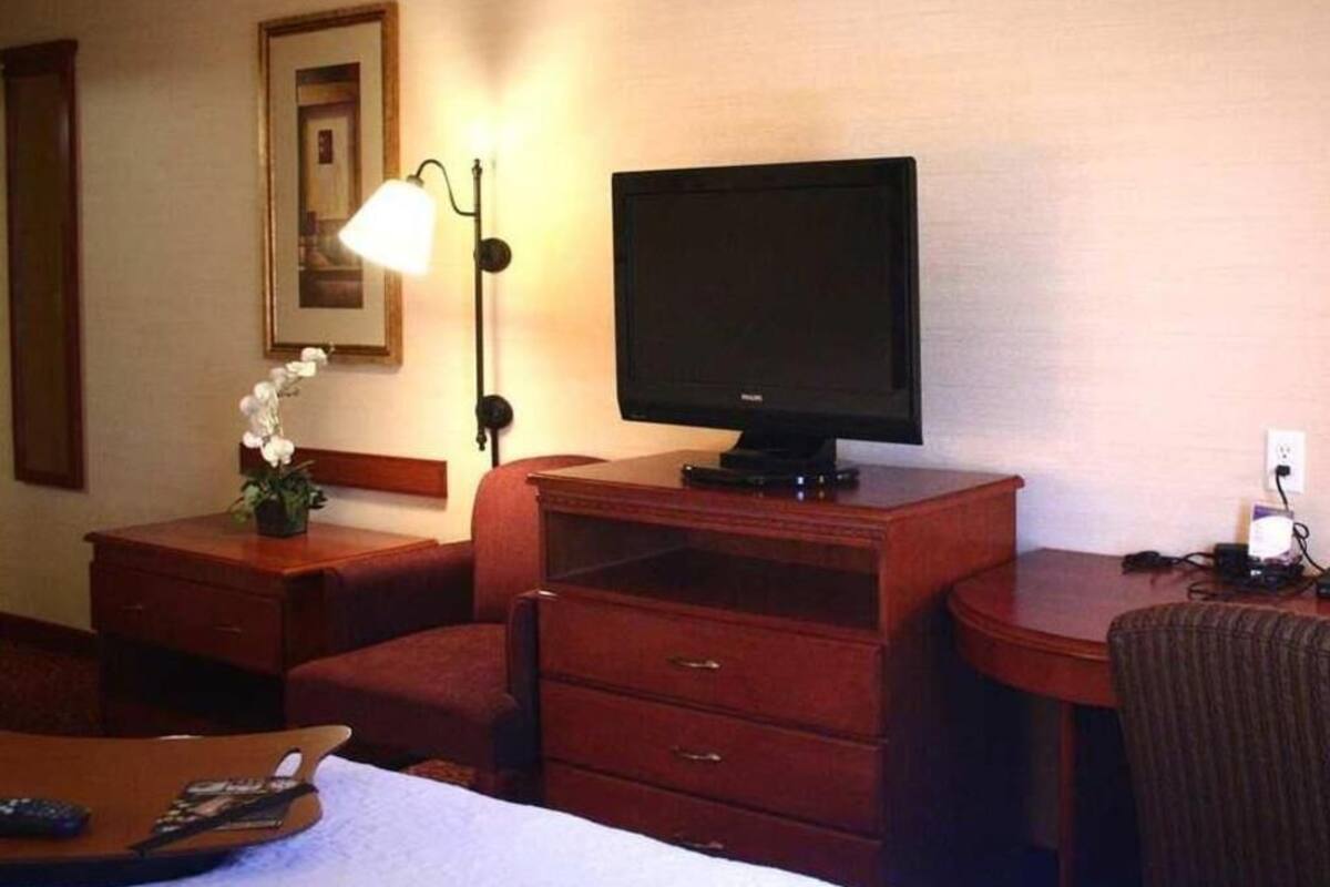 A hotel room with a bed, a desk with a computer, a TV, a lamp, and a chair.